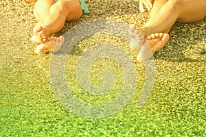 Vacation and summer holidays concept. Feet of two young girls relaxing on beach enjoying sun and sea on sunny day