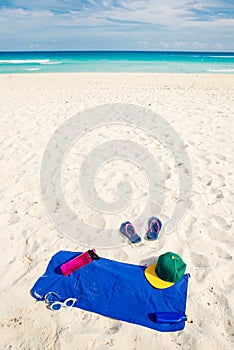 Vacation and summer holidays concept - flip flops, towel, cap, bottled water and bottle of sunscreen oil on beach sand
