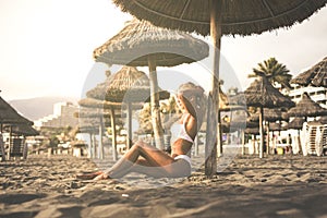 Vacation and sunbath concept. with beautiful blonde young girl sitting on the sand at the beach in resort - travel summer holiday