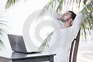 Vacation and technology. Work and travel. Young bearded man using laptop computer while sitting at beach cafe bar.