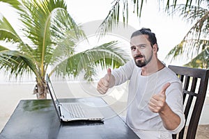 Vacation and technology. Work and travel. Young bearded man using laptop computer while sitting at beach cafe bar and
