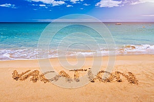 Vacation text on a beach. Vacation written in a sandy tropical beach. Vacation written in the sand on the beach blue waves in