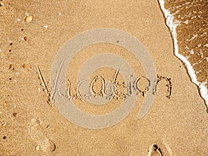 Vacation text written on sandy beach with wave near sea. Summer