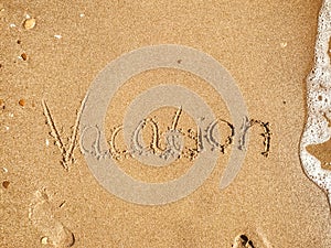 Vacation text written on sandy beach with wave near sea. Summer
