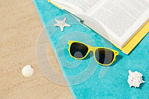 Sunglasses and book on beach towel on sand