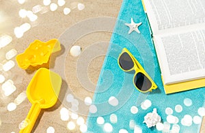 Sunglasses, sand toys and book on beach towel