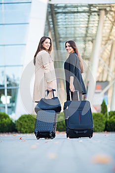 Vacation. Two happy girls traveling abroad together, carrying suitcase luggage in airport