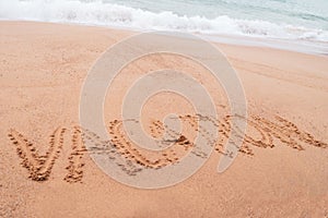 Vacation word hand drawn on sand summer beach