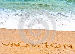 Vacation word written in the sand on the beach blue waves in the background