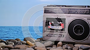 vacationer put on stone beach old vintage retro radio tape recorder and puts on audio cassette with sign relax. concept