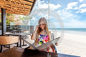 Vacationer at table facing sea, reading menu