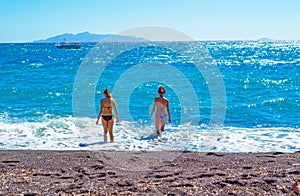 Vacationer women enter the sea at Black Beach Santorini Greece