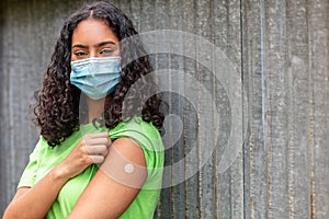 Vaccinated African American female young woman wearing face mask and vaccine band aid