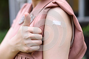 Vaccinated Woman Gesturing Thumb Up and Showing Arm With Plaster Bandage After Coronavirus Vaccine Injection.