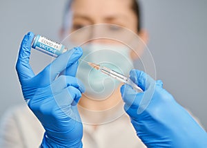 Vaccination against covid-19. A doctor in blue gloves holds a syringe and an ampule with a vaccine.