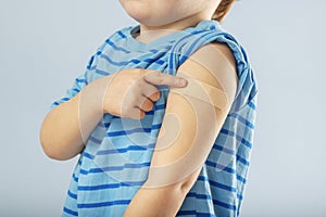 Vaccination of children. Vaccinated kid boy showing arm with adhesive bandage after vaccine injection. Kids and covid-19
