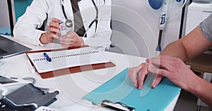 Vaccination concept. Close-up doctor in lab coat, stethoscope offers medication flask to patient at clinic office table.