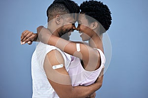 Vaccination, hug and black couple with plaster on arm in studio for cure, healthcare or booster shot on blue background