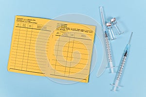 Vaccine concept with syringes, vials and empty yellow international certificate of vaccination on blue background