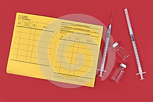 Vaccine concept with syringes, vials and empty yellow international certificate of vaccination with German and English text