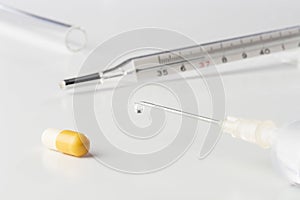 Vaccine droplet on medical syringe needle, thermometer, pill and tube on white