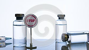 Vaccine side effect concept: a stop sign next to some vial and a syringe silhouette on reflective surface