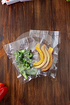 Vacuum bags with broccoli and pumpkin slices on a dark wooden table