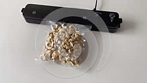 Vacuum packaging machine and vacuum bagged nuts. Device for packing food on a white table with a plastic cashew bag. The