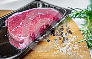 Vacuum-packed beef steak and spices on wooden chopping board