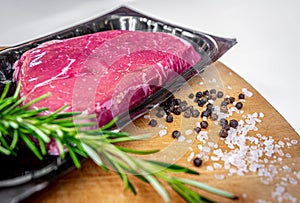 Vacuum-packed beef steak and spices on wooden chopping board