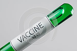 Vacuum tube with a sample of Covid-19 vaccine of green color in the hand with a medical glove
