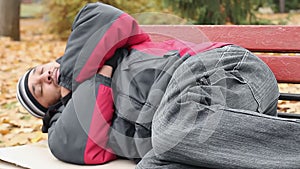 Vagabond in jacket and jeans sleeping on bench, trying to keep warm, poverty