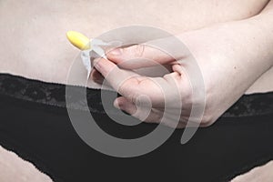 Vaginal or rectal candle in the hands of a woman against the background of the abdomen and underwear. The drug is in the form of