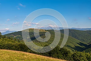Valcan mountains covered by deeo forest with meadows and rocks on upper partts of hills and higher Retezat mountain range on the photo