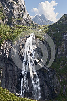 Valefossen waterfall flows vigorously down the cliffs of Lofoten Islands, Norway, amidst lush foliage