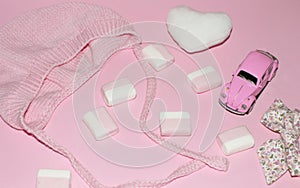 Valentine baby girl minimal pink background. Baby accessories: soft heart knitted hat  sweets  toy car and bow.Flat lay