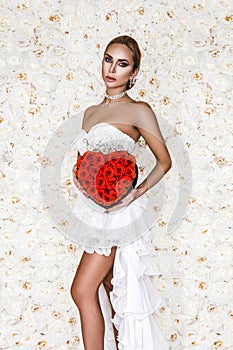 Valentine beautiful girl with red heart  on flowers background. Beautiful Happy Young woman in white elegant dress.