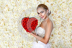 Valentine beautiful girl with red heart isolated on flowers background. Beautiful Happy Young woman in white elegant dress.