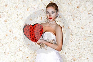 Valentine beautiful girl with red heart isolated on flowers background. Beautiful Happy Young woman in white elegant dress.