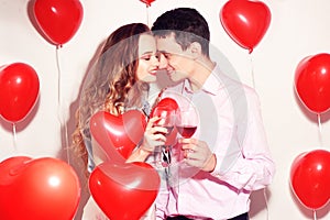 Valentine Beauty couple with red air balloons heart drinking red wine. Beautiful Happy Young woman and man hugs. Joyful lover