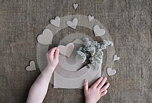 Valentine card in natural earth tone colors. Childs hands holding craft paper envelope with dried flowers and cardboard handmade