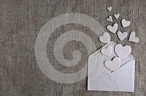 Valentine card in natural earth tone colors with copy space. Craft paper envelope with cardboard handmade hearts on canvas burlap