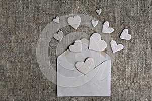 Valentine card in natural earth tone colors. Craft paper envelope with cardboard handmade hearts on canvas burlap background.