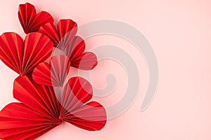 Valentine day background with red paper ribbed hearts as abstract shape on soft light pink background as festive backdrop.