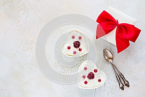Valentine day decoration, breakfast, yogurt with berries for two in white heart-shaped bowls and gift box on the table.