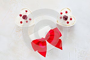 Valentine day decoration, breakfast, yogurt with berries for two in white heart-shaped bowls and gift box on the table
