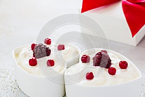 Valentine day decoration, breakfast, yogurt with berries for two in white heart-shaped bowls and gift box on the table