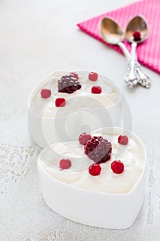 Valentine day decoration, breakfast, yogurt with berries for two in white heart-shaped bowls on the table