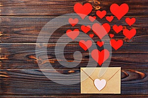 Valentine day love letter. Envelope from craft paper with red hearts heap spread on white wood background. Lover`s holiday confes