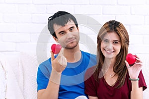 Valentine day. Love and relationships concept. smile young couple sitting on white couch holding red heart in their hands